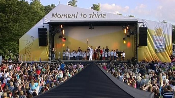 The Olympic torch is held aloft on stage.