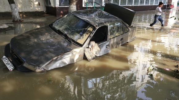 A local resident passes by a damaged car stuck in a flooded street in the town of Krymsk