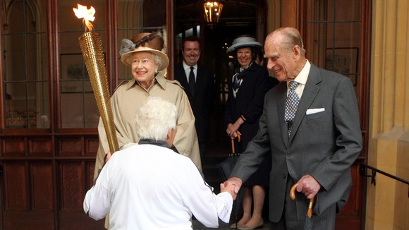 The Queen looks at the Olympic flame as the Duke of Edinburgh shakes hands with torchbearer Gina Macgregor at Windsor Castle.