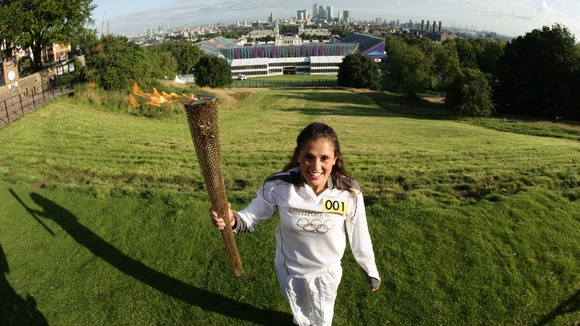 Natasha Sinha holding the Olympic Flame on the Torch Relay leg in front of the Olympic Equestrian Arena next to the Greenwich Naval Collage.