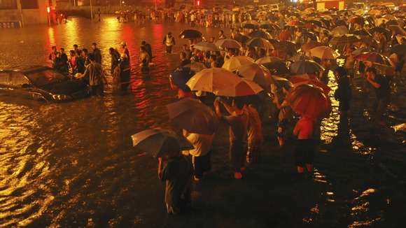 car submerged in floodwater as people look on