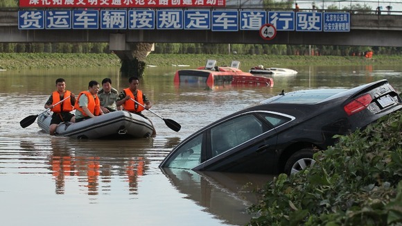 A rescue boat approaches a partially submerged car on a flooded highway after heavy rainfalls in Beijing