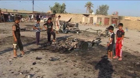 Children stand around the site of a car bomb attack in Mahmudiya, Iraq