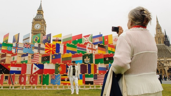 Tourists pose for photographs next to an artwork of national flags in Westminster