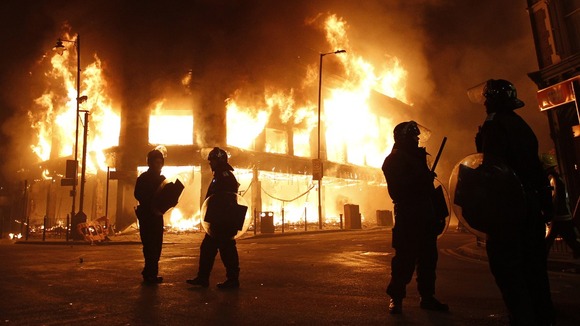 Police officers wearing riot gear stand in front of a burning building in Tottenham, north London August 7, 2011.