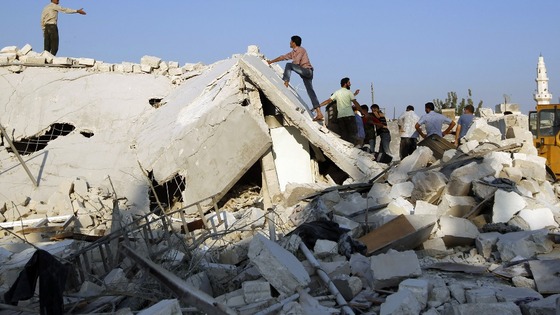 People stand on a house destroyed during a recent Syrian Air force air strike in Azaz