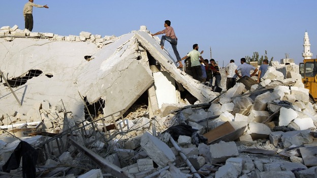 People stand on a house destroyed during a recent Syrian Air force air strike in Azaz