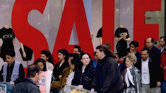 Shoppers make their way past a large sale sign in a shop window on Oxford Street.