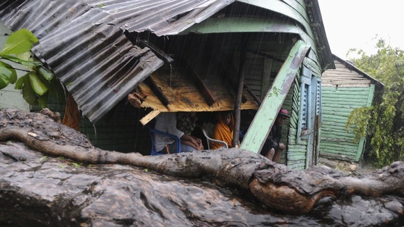 A family sits in their porch after winds from Tropical Storm Isaac brought a tree down, hitting the corner of their house, in El Habanero