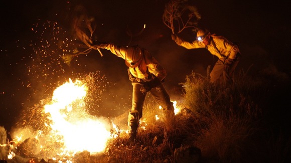 Firefighters try to extinguish a fire with branches in a forest at Barranco Blanco in Coin