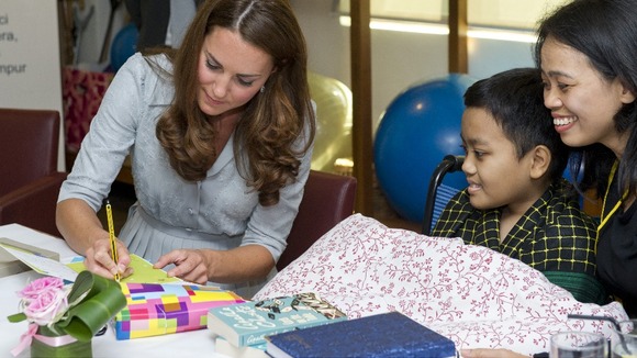 The Duchess of Cambridge signs a birthday card for Zakwan Anuar, 15, watched by his mother.