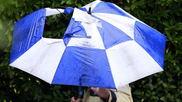 A man with a broken umbrella walks through Stockport.