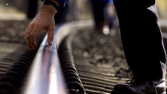 An engineer checks part of the West Coast train line with his hand.