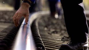 An engineer checks part of the West Coast train line with his hand.